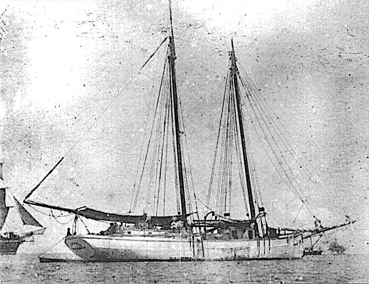 Old black-and-white photograph of a two-masted schooner at anchor in a tropical harbor