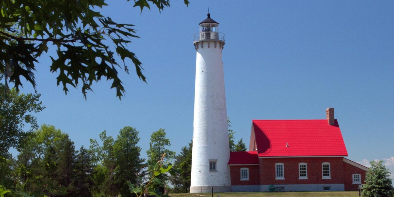 White Tawas Point Lighthouse tower and red-roofed keeper's house among trees on Saginaw Bay