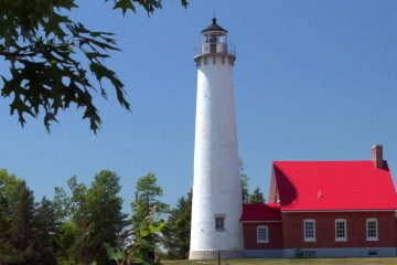 White Tawas Point Lighthouse tower and red-roofed keeper's house among trees on Saginaw Bay