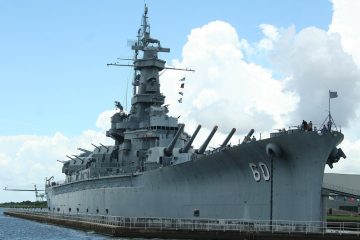 Gray battleship USS Alabama, hull number 60, berthed at Battleship Memorial Park in Mobile Bay under billowing clouds