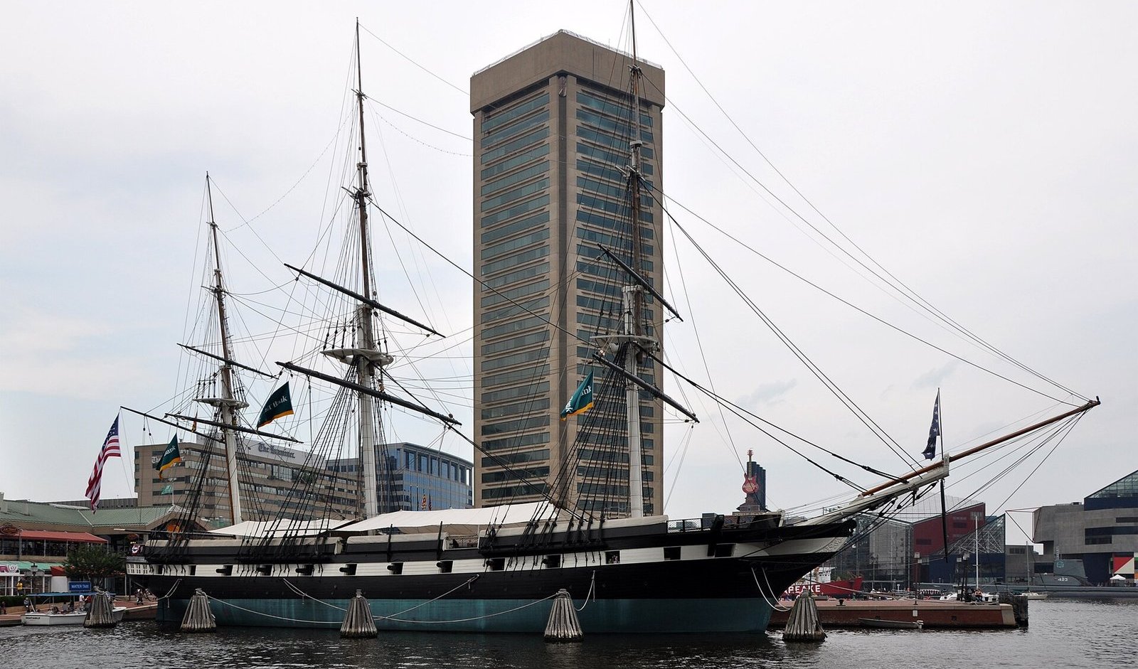 Sloop-of-war USS Constellation with tall masts and rigging moored in Baltimore Inner Harbor beside a high-rise tower
